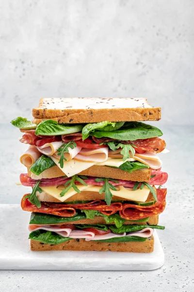 Big tasty sandwich with ham, salami, salad, cheese and tomatoes — Stock Photo, Image