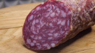 Tahta kesme tahtasının üzerinde tütsülenmiş bir sosis parçası. Yakın çekim video. Yarım sosis..