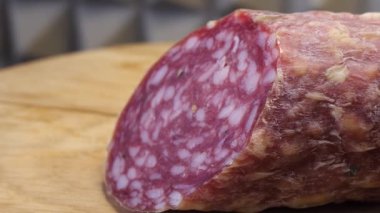 Tahta kesme tahtasının üzerinde tütsülenmiş bir sosis parçası. Makro video. Yarım sosis..