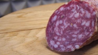 Tahta kesme tahtasının üzerinde tütsülenmiş bir sosis parçası. Makro video.
