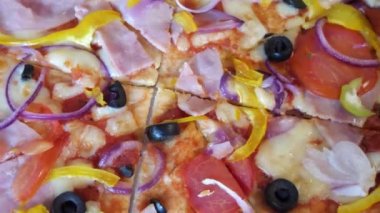 Zeytinli, domatesli ve jambonlu pizza. Kapalı çekimli video. Dönen pizza, tam kare görüntü. İtalyan yemeği, makro video.