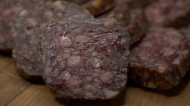 Pieces of salami on a wooden surface, close-up video. Delicious appetizer. Soft focus
