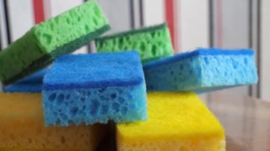 Multi-colored washcloths for washing dishes and cleaning on a rotating surface, macro video. Green, blue and yellow sponges.