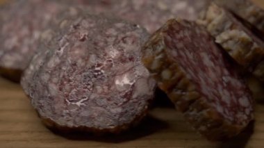 Pieces of salami on a wooden surface, close-up video. Delicious appetizer.