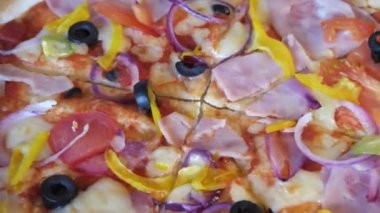 Zeytinli, domatesli ve jambonlu pizza. Kapalı çekimli video. Dönen pizza, tam kare..