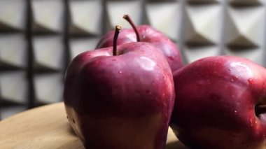 Kırmızı şefin üç ıslak kırmızı elması gri bir duvara karşı dönen ahşap bir yüzey üzerinde, yakın plan video. Olgun sulu meyveler.