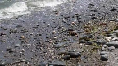 Islak taş çakıl taşları ve kıyı dalgaları. Suda beyaz köpük. El bilgisayarı videosu.