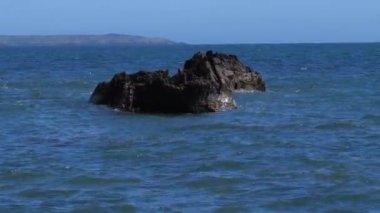 Bir günde sakin bir deniz yüzeyi. Suda büyük kayalar var. El bilgisayarı videosu.