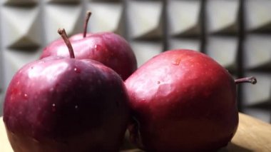 Three wet red apples of the red chief variety on a rotating wooden surface against a gray wall, video. Ripe fruits close-up.