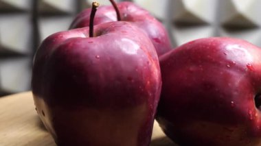 Kırmızı şefin üç ıslak kırmızı elması gri bir duvara karşı dönen ahşap bir yüzey üzerinde. Olgun meyveler yakın plan.