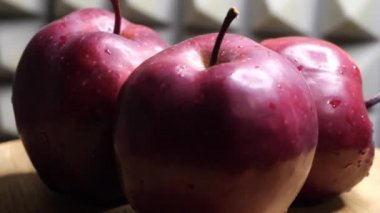 Three wet red apples of the red chief variety on a rotating wooden surface against a gray wall. Ripe fruits.
