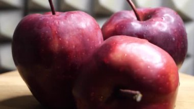 Three wet red apples of the red chief variety on a rotating surface against a gray wall. Ripe fruits.