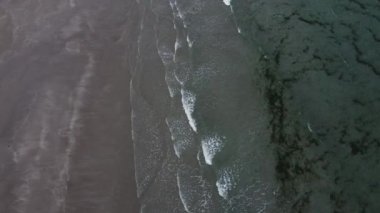Tidal waves of the Atlantic Ocean and a beautiful sandy beach, video from the top. Green algae in seawater. Cool coast of the North Atlantic. Seascape.