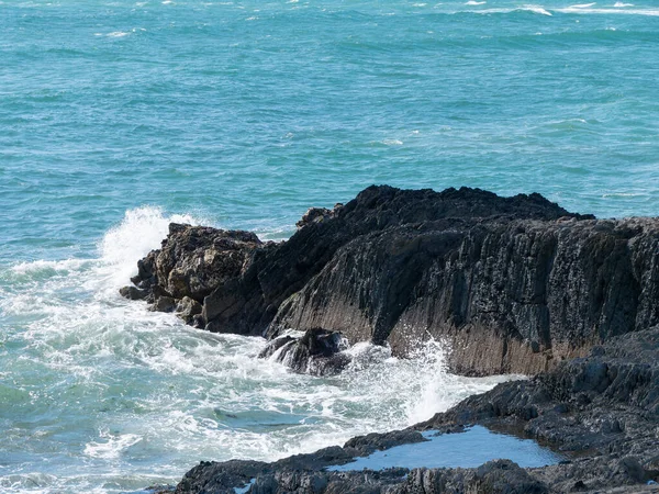 Tidal waves break on coastal rocks, seascape. The water is turquoise in color. White foam on the waves, splashes, rock beside sea.