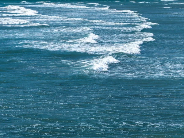 Beautiful foam on turquoise tidal waves. The surface of the water as a background. Blue ocean water