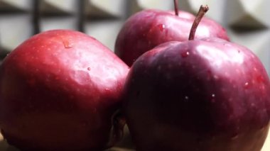 Three wet apples of the red chief variety on a rotating surface against a gray wall. Ripe fruits.