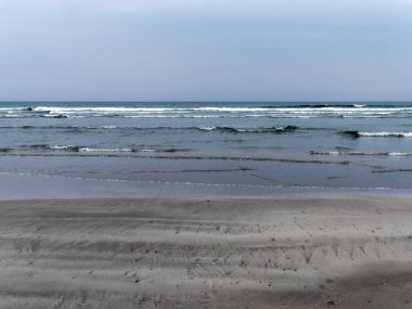 The shore of the Celtic Sea at low tide. Wet sandy beach on a cool day. Minimalistic seascape. Cloudy cool weather.