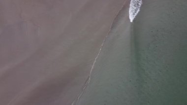 Tidal waves roll over the sandy shore. Deserted beach, aerial view. Coastline on a cloudy day, background.