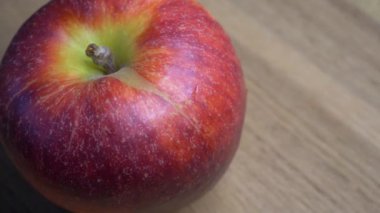 Big apple of the Gala variety on a wooden surface, 4k macro video resolution. The bitten apple rotates. A place for the text, a copy space.