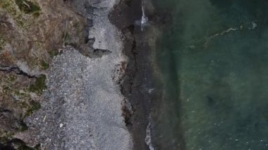 Okyanus dalgalarının insansız hava aracı tarafından çekilen üst hava görüntüsü kayalık bir dağın yüksek uçurumunda kırılıyor. İHA 'nın sahil dalgaları görüntüsü, temiz su. Kayalık bir sahilde dalgalar