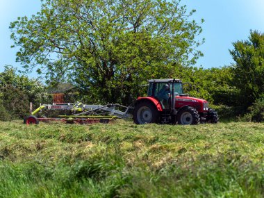 West Cork, İrlanda, 28 Mayıs 2022. Bir traktör hayvan yemi için saman toplar. Bir kaplıcada tarım işindeyim, tarım işindeyim. Yeşil çimenlikte kırmızı ve siyah traktör