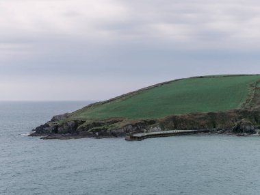 Warren plajındaki sahil kayalıklarının manzarası. İrlanda 'nın güneyindeki kayalık kıyılarda. Bir bahar günü gökyüzünün altındaki tepeler, denizin yanındaki dağlar bulutların ve gökyüzünün altında.