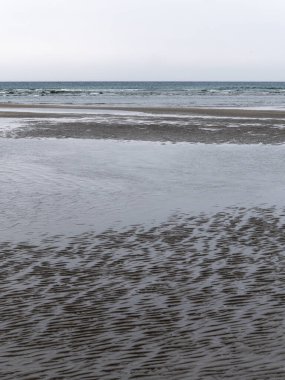 Kıyıda ıslak kum, alçak gelgit. Kasvetli deniz manzarası. Kuzey Avrupa 'nın sert doğası. Atlantik Okyanusu 'nun soğuk kıyıları. Gri kumsal