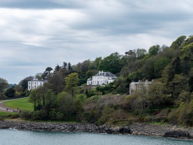 Körfezin kıyısında bir tepe. Tepede birkaç bina ve ağaç var. Glandore, İrlanda 'nın güneyinde bir köydür. Gökyüzünde güzel bulutlar, dramatik manzara.