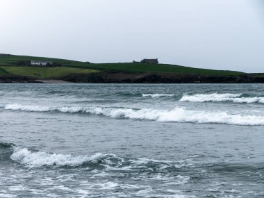 Deniz yükseldiğinde. Deniz kıyısındaki bir tepede bir bina. Gri kasvetli gökyüzü, deniz kenarındaki yeşil çimlerin üzerine inşa ediliyor. Deniz manzarası, dalgalarda beyaz köpük.
