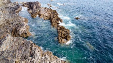 Kıyıdaki kayalarda güzel deniz dalgaları kopuyor. Turkuaz suda beyaz köpük. Güneşli bir günde deniz manzarası.