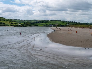 West Cork, İrlanda, 12 Haziran 2022. Bulutlu bir yaz gününde Inchydoney plajı. Ünlü İrlanda plajında birçok turist vardır. Deniz kıyısında bir tatil köyü. Avrupa deniz manzarası. Sahildeki insanlar