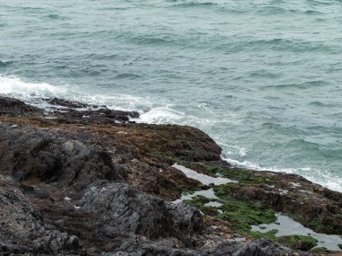 Soğuk deniz suyu ve kıyı kayaları. Atlantik kıyısında bulutlu bir hava. Sörf ve beyaz deniz köpüğü, suyun yanında kaya oluşumu..