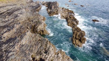 Güzel dalgalar kayalarda kırılır. Turkuaz suda beyaz köpük. Güneşli bir günde deniz manzarası.