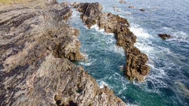 Güzel dalgalar kayalarda kırılır. Suda beyaz köpük. Güneşli bir günde deniz manzarası.