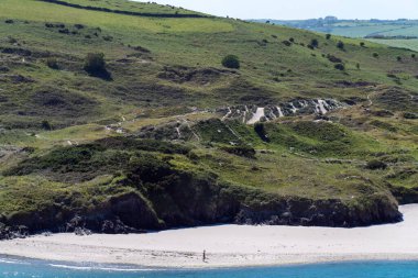 County Cork, İrlanda, 28 Mayıs 2022. Bir bahar günü Atlantik Okyanusu kıyısında çalılarla kaplı kum tepeleri. Bir beyaz adam deniz kıyısında yürüyor. Mavi denizin kıyısındaki yeşil çimenler