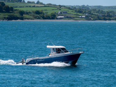 County Cork, İrlanda, 28 Mayıs 2022. Güneşli bir bahar gününde mavi bir denizde beyaz ve mavi bir motorlu tekne yol alıyor. Deniz Burnu. Denizde beyaz ve mavi bir tekne
