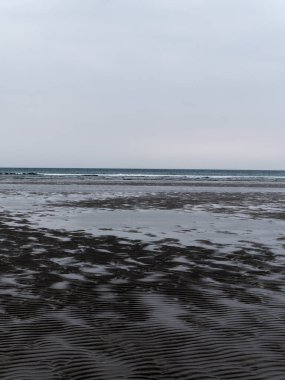 Bulutlu bir günde deniz kıyısında ıslak dalgalı kum. Kasvetli deniz manzarası. Kuzey Avrupa 'nın sert doğası. Atlantik Okyanusu 'nun soğuk kıyısı, plaj..