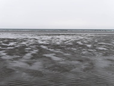 Bulutlu bir günde deniz kıyısında ıslak dalgalı kum. Kasvetli deniz manzarası. Kuzey Avrupa 'nın sert doğası. Atlantik Okyanusunun soğuk kıyıları.