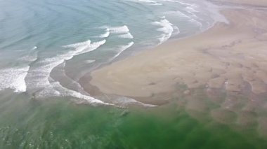 Islak kum ve güzel gelgit dalgalarıyla ıssız bir sahil. Dalgalarda beyaz deniz köpüğü. Deniz manzarası, İHA videosu. Atlantik Okyanusu 'nun yüzeyindeki dalgalar, gelgit..