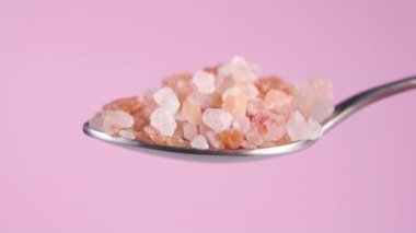 Himalaya kaba kaya tuzu renkli pembe bir arka planda kaşıkta. Düşen portakal kristalleri. Makro. Yavaş çekim