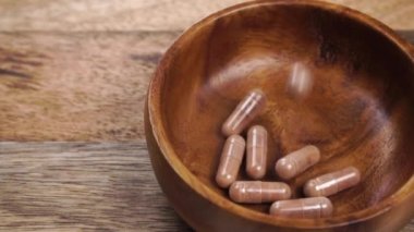 Kahverengi tıbbi kapsüller ahşap bir kaseye, eski bir ahşap şarap masasında düşer. Ağır çekim. Kapatın. Tıp konsepti. Antiviral haplar