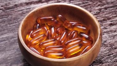 Omega-3 kapsülleri ahşap bir kapta, ahşap bir yüzey üzerinde. Yabani somon balığı yağlı sarı turuncu haplar. Sağlık hizmetleri takviyeleri. Klasik manzara. Döndürme. Kapat.