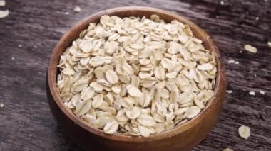 Tahta bir kase kuru yulaf ezmesi ahşap bir yüzey üzerinde döner. Pişmemiş yulaflar sağlıklı vejetaryen yemekleri