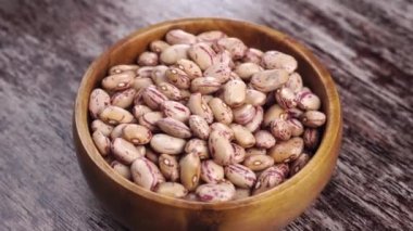 Kırsal bir ahşap yüzey üzerinde ahşap bir kasede pişmemiş kuru yaban mersini fasulyesi. Döndürme. Kapatın. Sebzeli sağlıklı yiyecek.