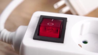 Finger beyaz bir elektrik uzatma kablosunu kapatıyor, düğmeye yakın basıyor. Elektrik tasarrufu kavramı. Kırmızı düğme. Elektrik prizi bulanık. Ahşap bir arka planda