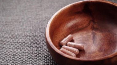 Tıbbi bitkisel kapsüller yavaş çekimde kırsal ahşap bir kaseye düşer. Kapatın. İlave haplar