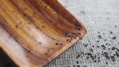 Kuru siyah susam tohumları ahşap mutfak gereçlerine yavaş çekimde kaba kaba bir jüt kumaş üzerinde düşer. Kapatın. Organik sağlıklı sesamum sosu.