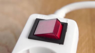 Parmak, beyaz elektrik şeridinin kırmızı düğmesine basıyor. Kapatın. Elektrik tedarik konsepti. Ahşap bir arka planda uzatma kablosu açmak