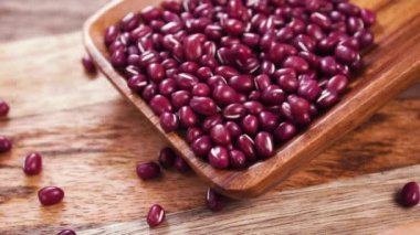 Kuru adzuki kırmızı fasulyeleri yavaş çekimde kırsal ahşap mutfak malzemelerinin üzerine düşüyor. Kapatın. Pişmemiş organik baklagiller. Vigna angularis