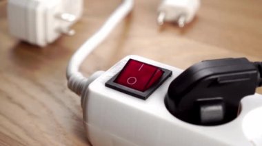 Ahşap bir arka planda uzatma kablosunu açmak. Parmak beyaz elektrik şeridinin kırmızı düğmesine basıyor. Kapatın. Elektrik tedarik konsepti. Bağlı siyah elektrik prizi